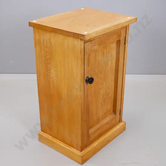 oak bedside cupboard with panelled door having black porcelain knob on plinth base