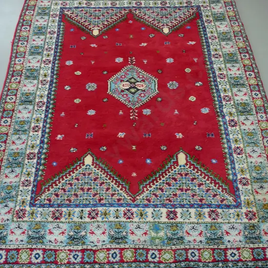 large woollen Turkish rug, red ground, central geometric medallion, multiple geometric borders in blue, red and white