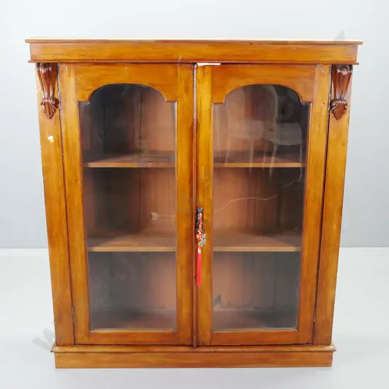 Victorian mahogany bookcase with 2 glazed arched panelled doors, carved corbels, 2 shelves, plinth base. Missing piece
