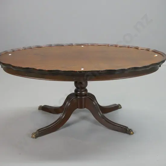 reproduction walnut oval coffee table with raised shaped edge, column base on 4 sweeping legs w/brass paw feet - top and
