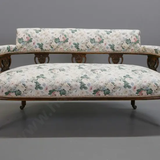 Edwardian beech 2-seater tub settee w/ carved back rail decoration, on turned legs and porcelain casters, some fading to