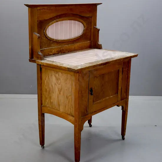 art deco oak wash stand with inset pink tiles in oval framed back and top, cupboard door with drop handle, on porcelain