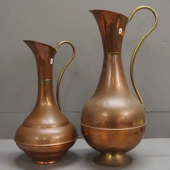 2 copper and brass ewer jugs with flared bases, one base is brass, one copper, both with a bit of wear, larger one has