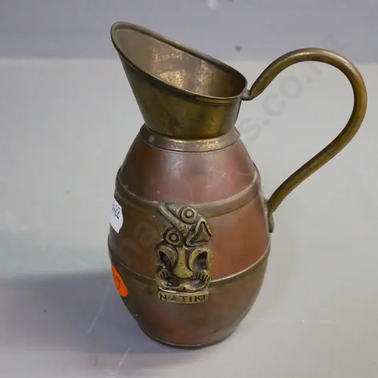 brass and copper jug with 'NZ Tiki' and applied brass Tiki, some dents. H-130, D-100