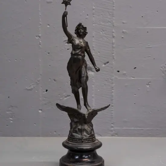 art nouveau maiden figure standing on an eagle holding a star, 'La Nuit'. Rounded wooden base with a plaque.