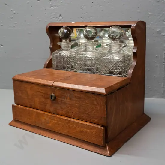 vintage oak tantalus with 3 decanters, lift-up lids exposing storage compartments, concealed latch for lower spring-