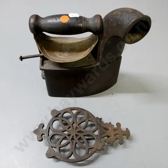 vintage cast metal coal iron on pierced trivet with embossed heat shield, turned wooden handle, back latch figurative.
