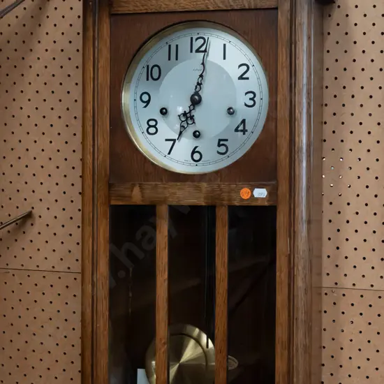 oak cased Art Deco chiming wall clock by Enfield, England. Glazed panels to door, brass pendulum and key. H-770 W-340