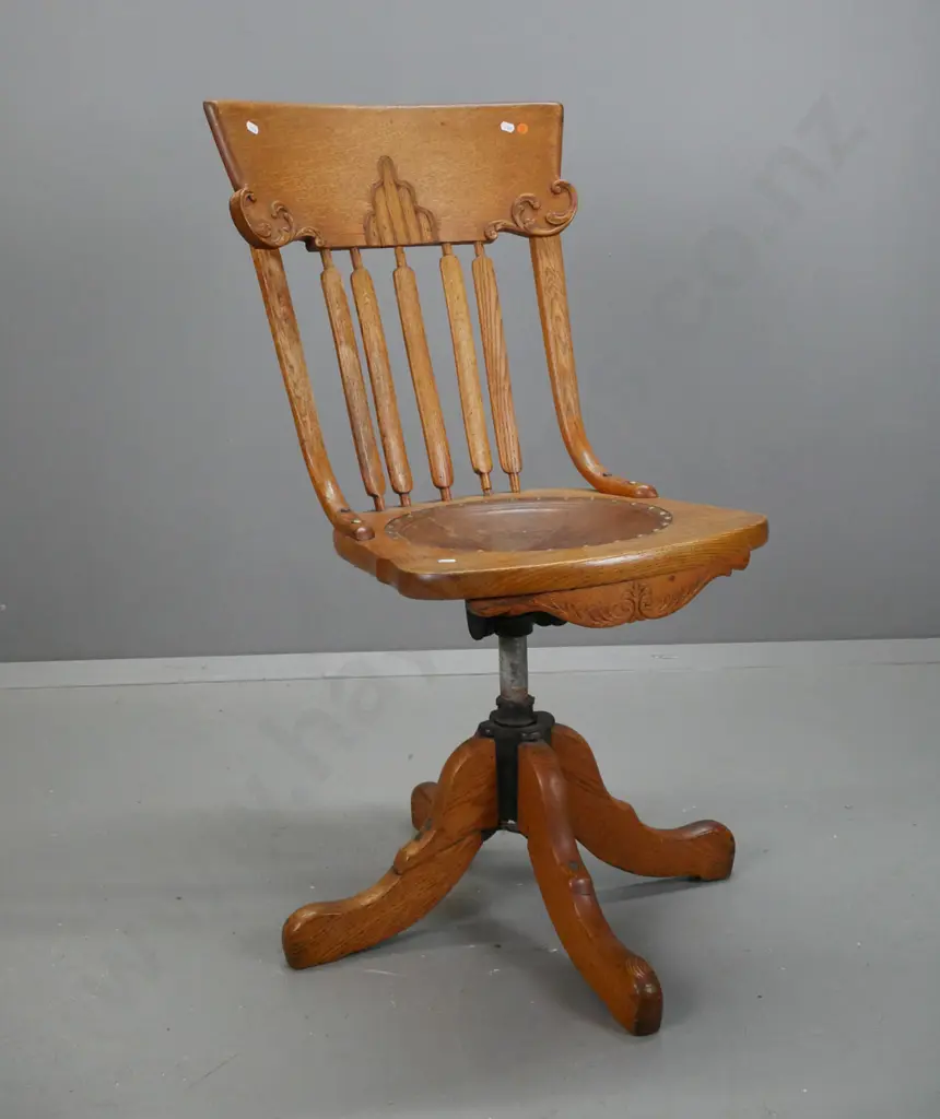 vintage revolving oak desk chair, slatted back w/ shaped crest, leather seat embossed wreath w/ helmet & sword. On 4-pt Image 1++