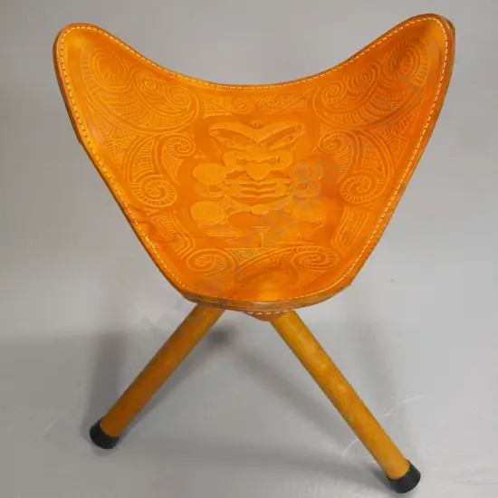collapsible tripod stool with Maori themed tooled leather seat - stitching coming loose on one corner H470 W-370